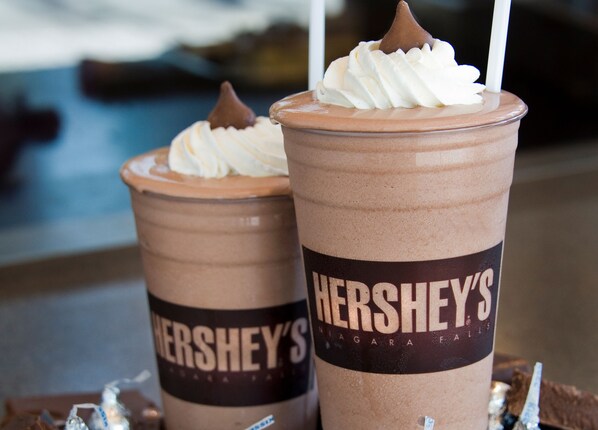 Two cups of chocolate milkshakes with whipped cream and a chocolate piece on top, labeled 'Hershey's'.