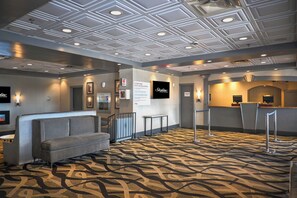Un hall d’hôtel avec un tapis à motifs, un canapé, un comptoir d’accueil et un écran de télévision.