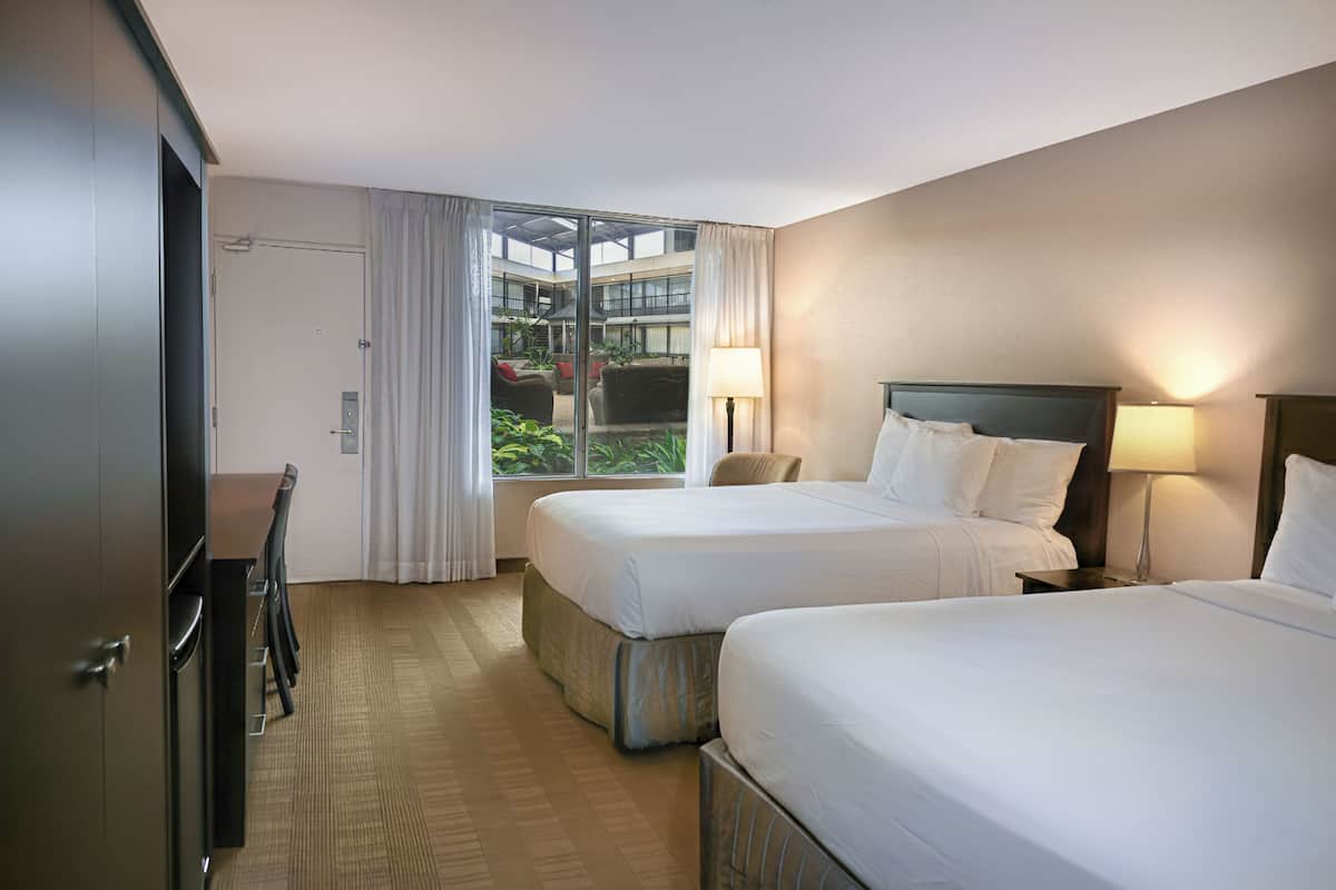 Ein Hotelzimmer mit zwei Betten, einem Schreibtisch und Blick auf einen Innenhof.