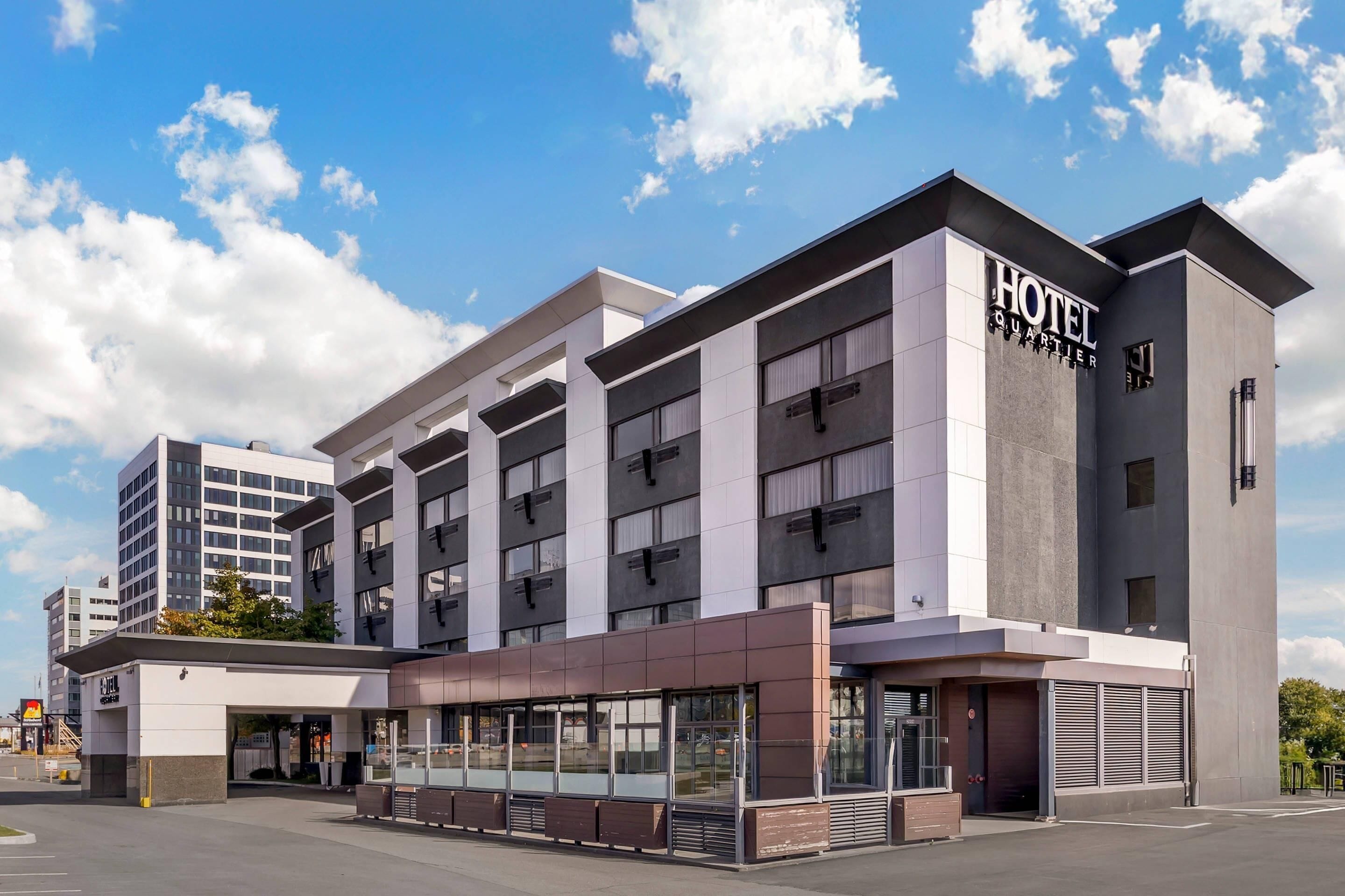 Un moderno edificio de hotel con un llamativo letrero que dice "HOTEL QUARTIER", grandes ventanales y un diseño de techo plano.