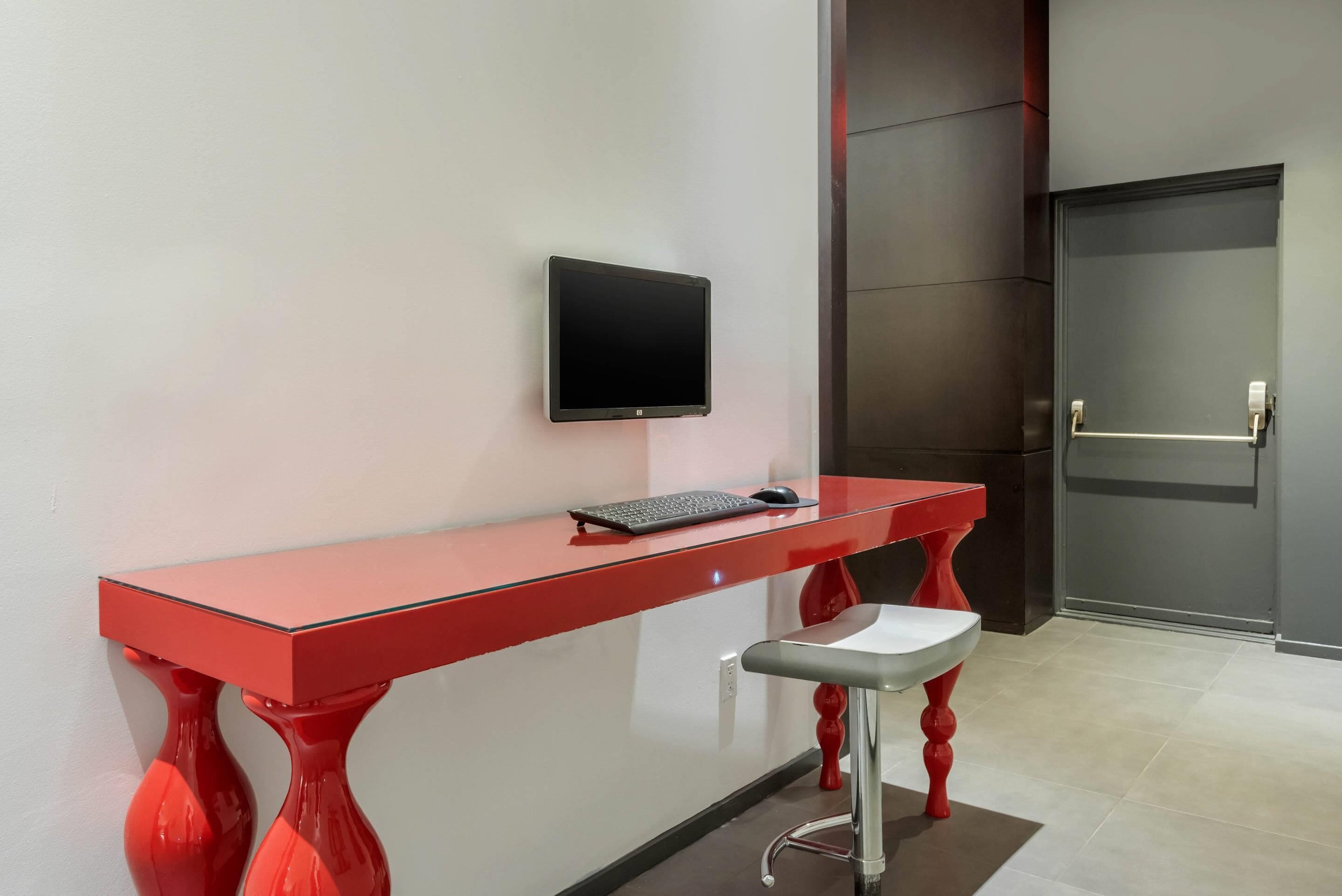A modern room with a red desk, a black monitor, and a red stool.