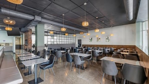 A modern restaurant with high ceilings, exposed ductwork, and pendant lighting. Tables and chairs are arranged for dining. - Hotel Quartier, an Ascend Collection Hotel (Québec City)