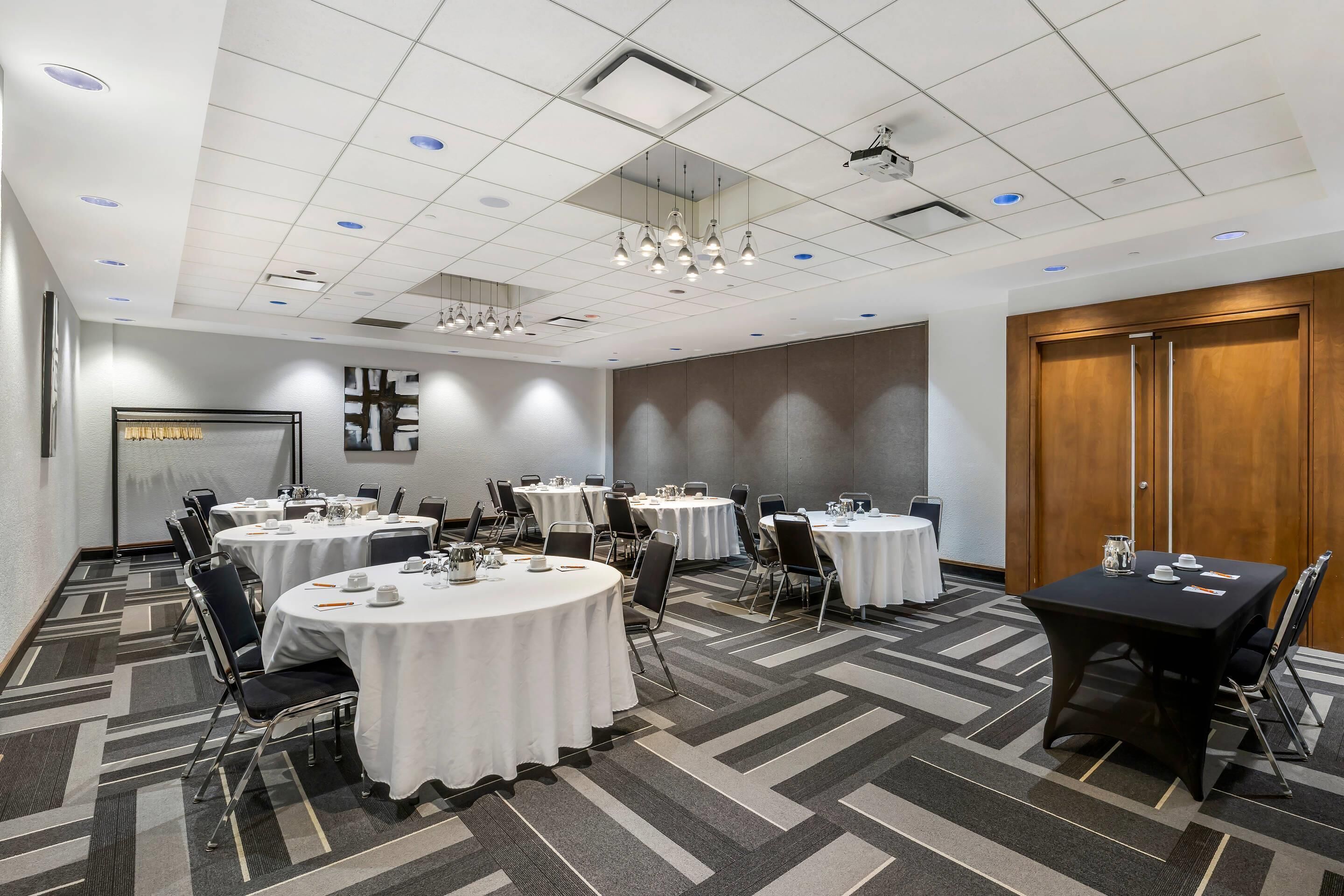 A conference room with round tables, chairs, and a projector screen.
