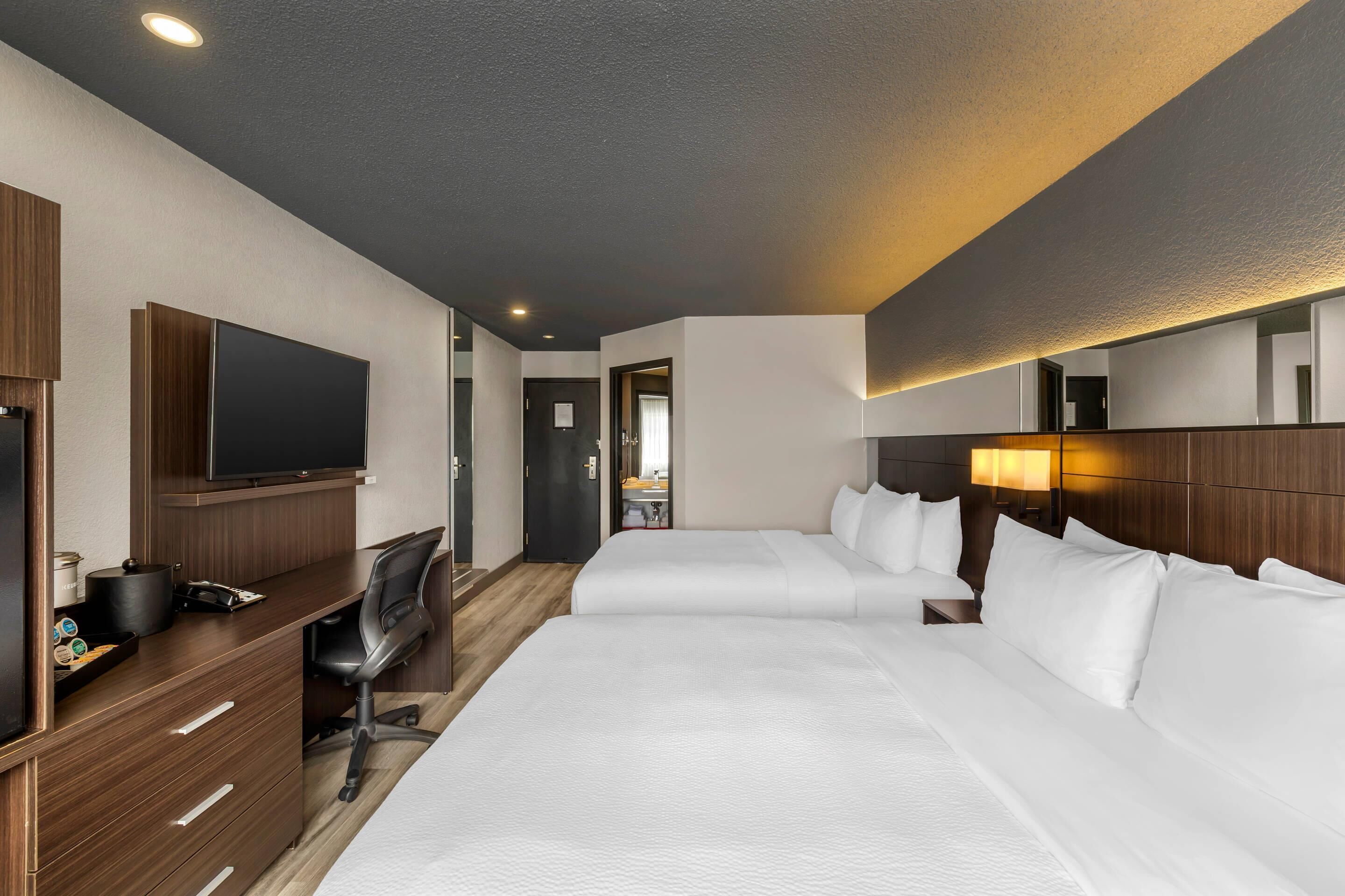 Una habitación de hotel con una cama grande, un escritorio con silla, una televisión y un espejo.
