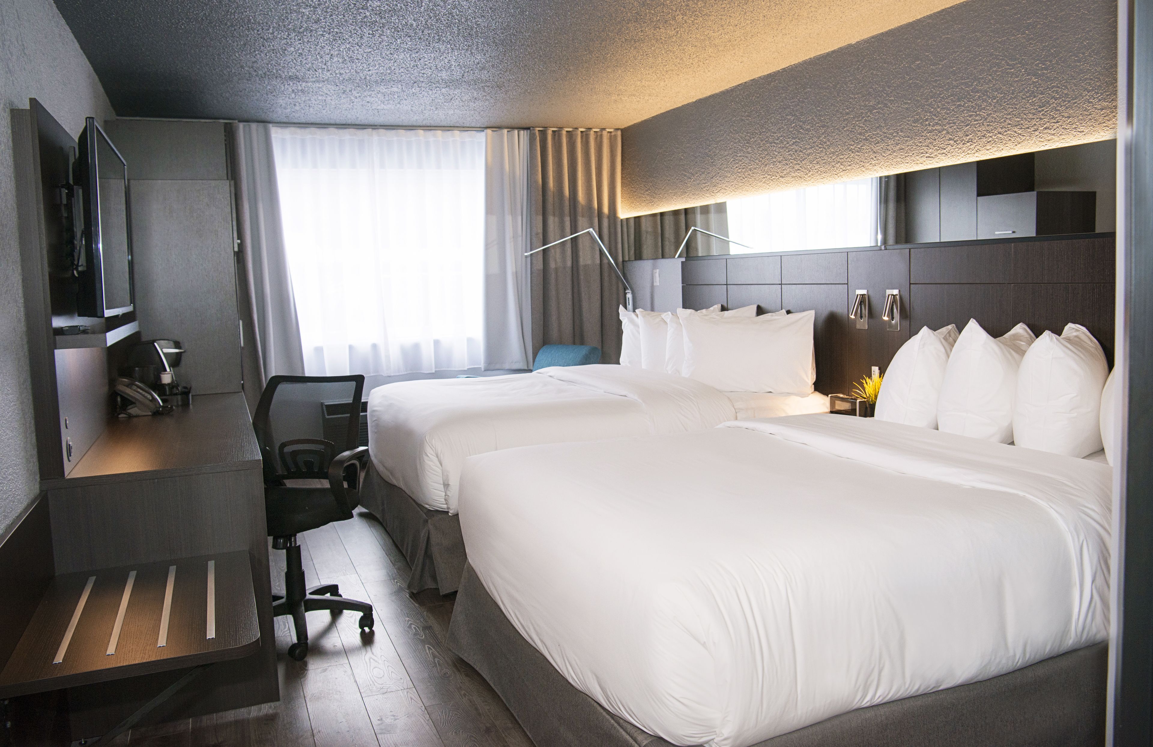 A hotel room with two beds, a desk, a chair, a TV, and a window with curtains.