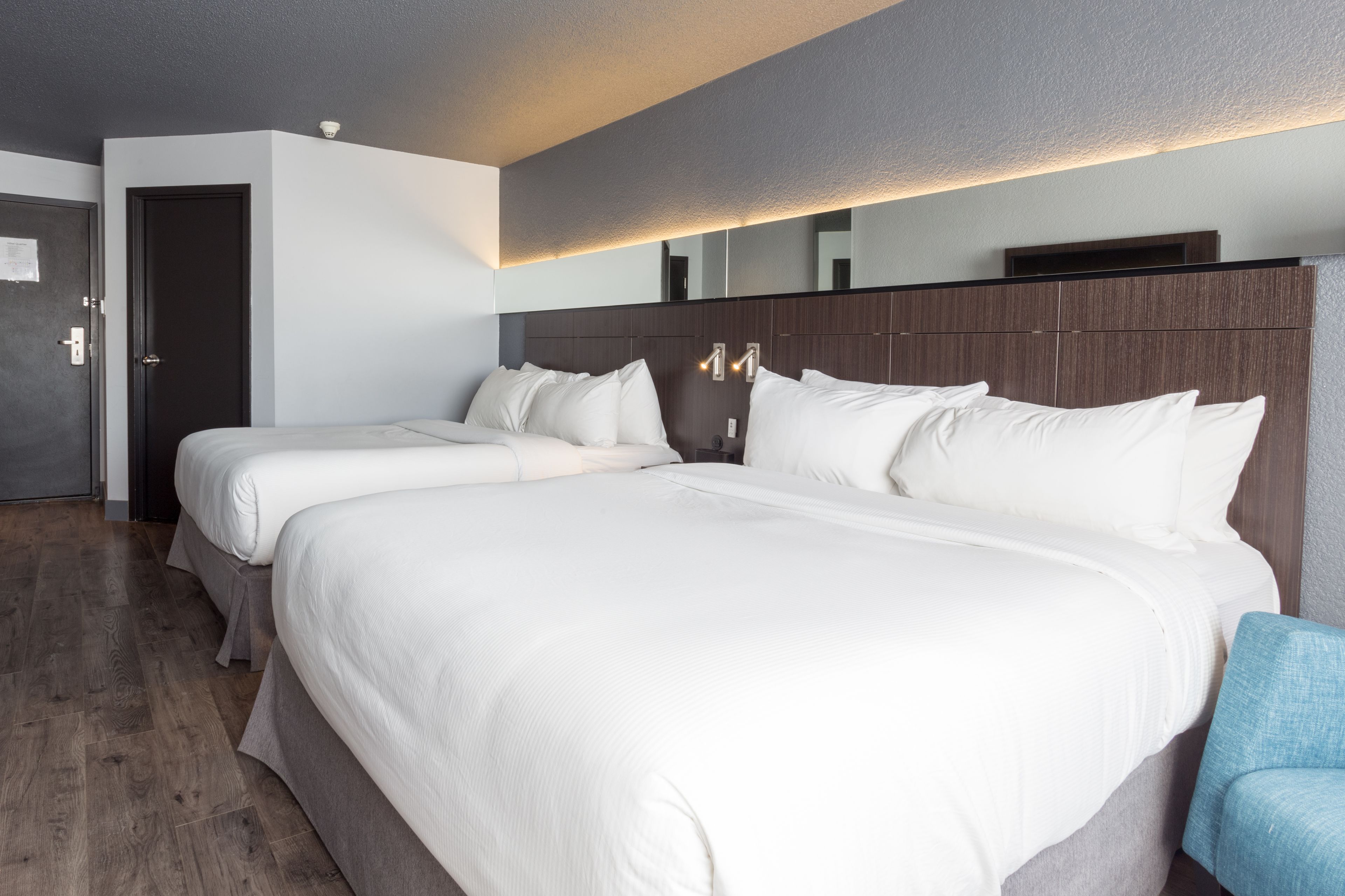 Habitación de hotel con dos camas, suelo de madera, puerta oscura y pared de color claro.