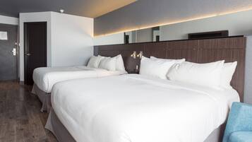 Habitación de hotel con dos camas, suelo de madera, puerta oscura y pared de color claro.