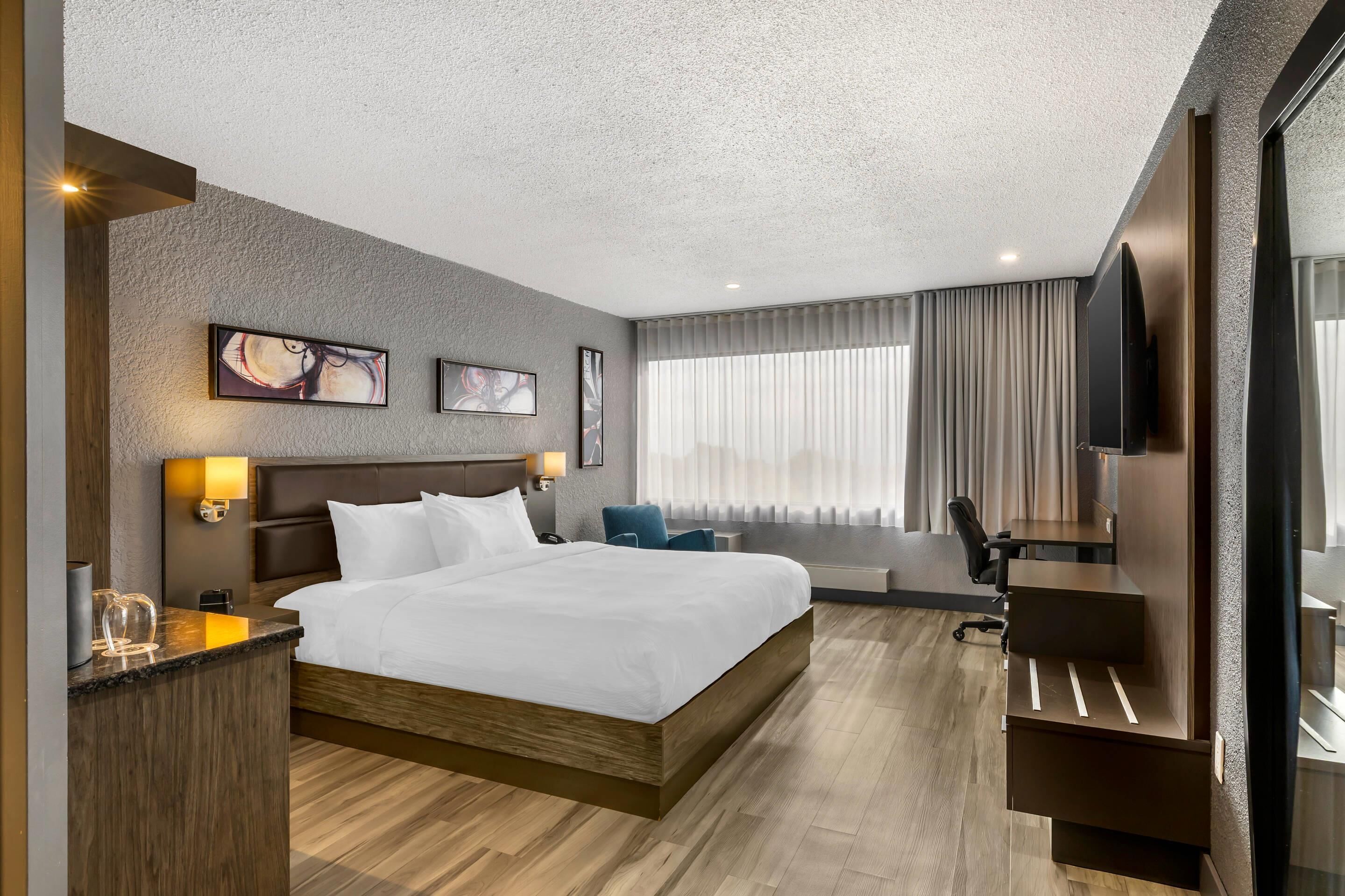 Habitación de hotel con una cama grande, un escritorio, una silla, un televisor y una ventana con cortinas.