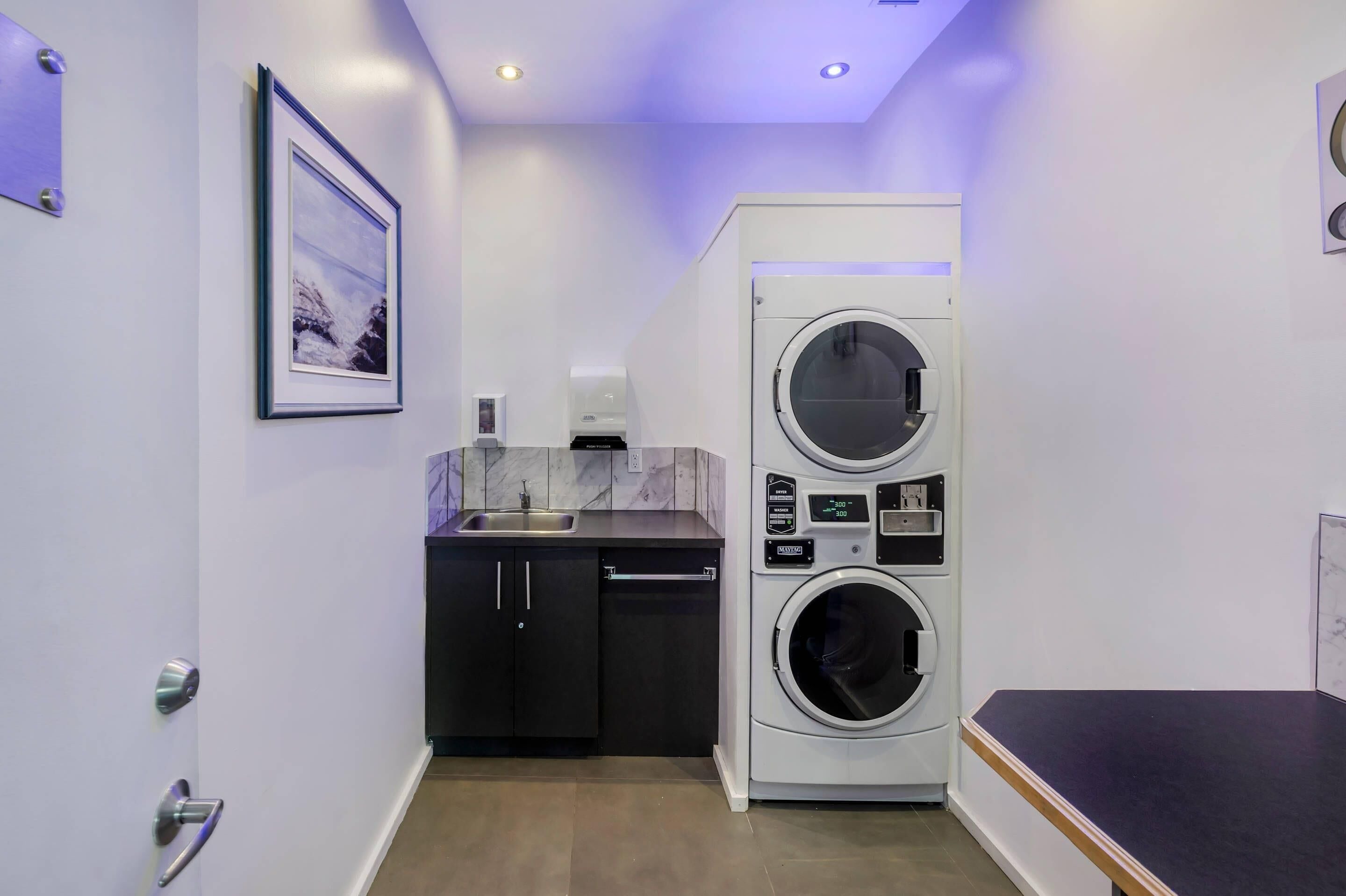 A compact laundry room with a washing machine and dryer, a sink, and a marble backsplash.