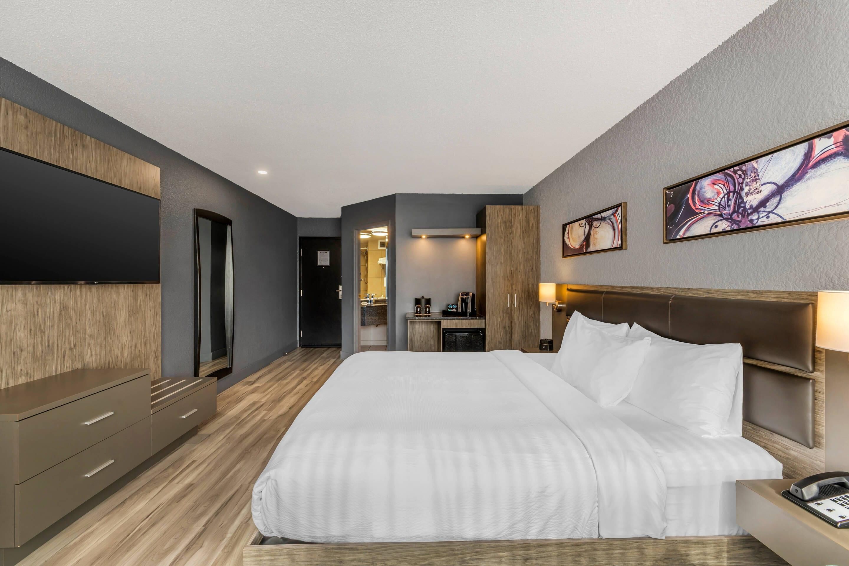 Una habitación de hotel moderna con una cama grande, un televisor de pantalla plana, un aparador de madera y un escritorio con lámpara.