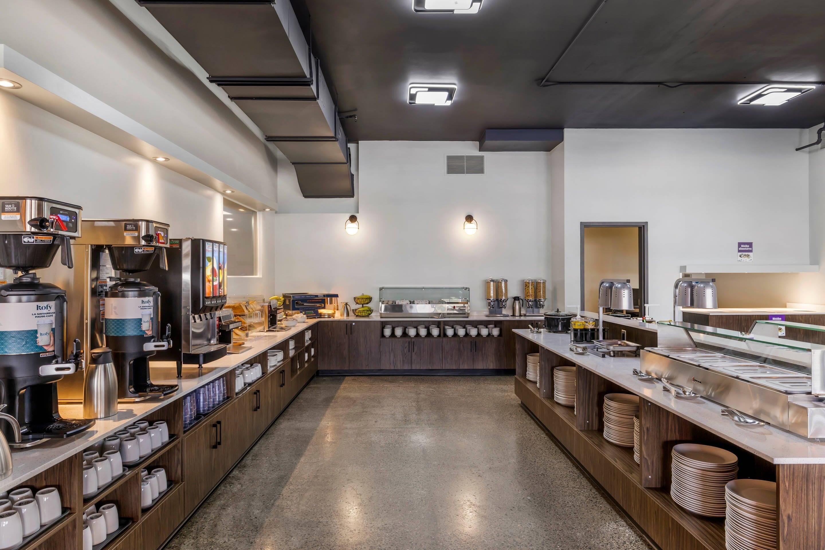 Un espace café moderne, doté de plusieurs machines à café et d’un buffet proposant une variété de plats et de boissons.