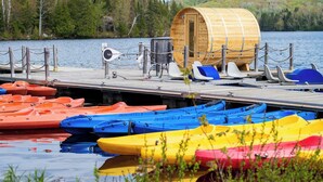 Eine Holzhütte mit Sauna, umgeben von einem Steg mit bunten Kajaks.