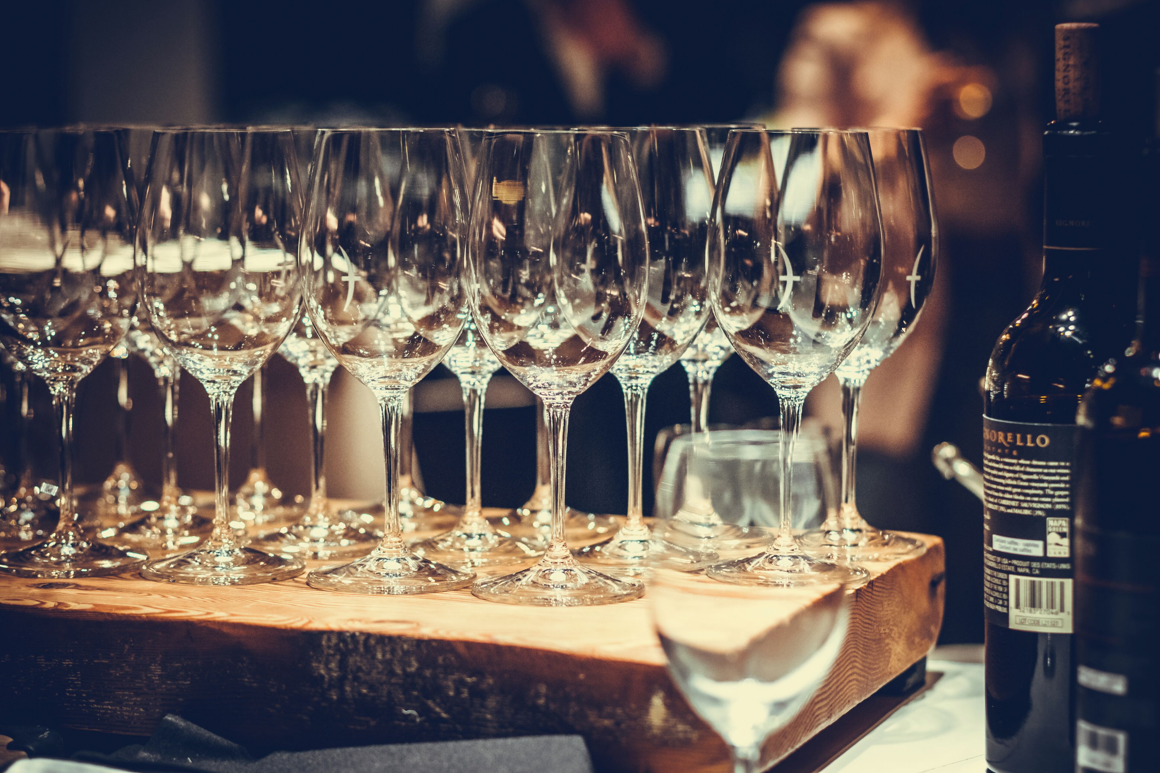 A row of empty wine glasses on a wooden table with a bottle of wine.
