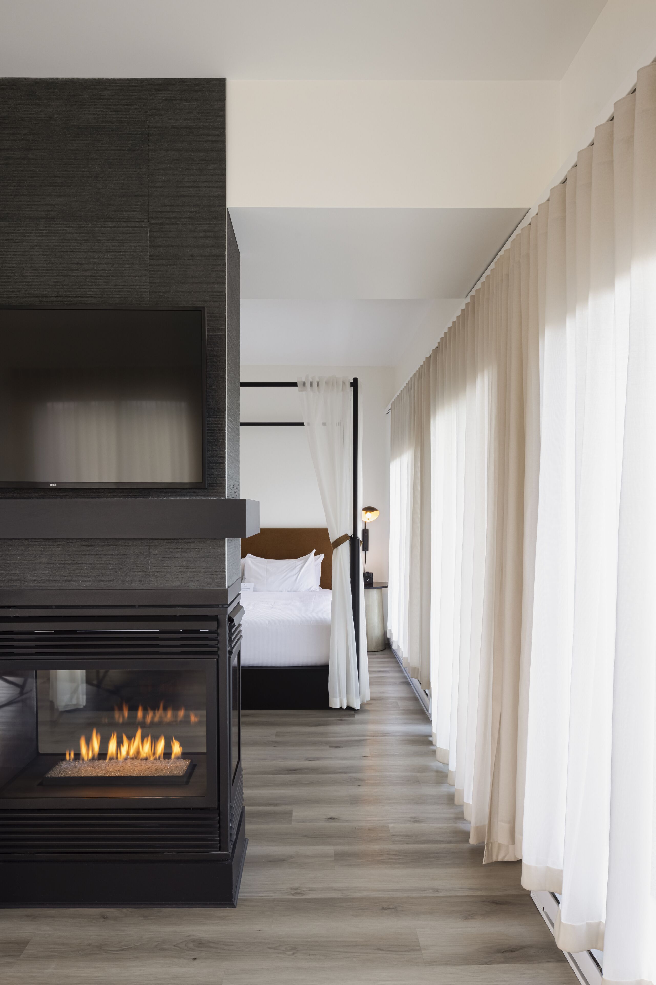 A modern hotel room with a fireplace, a bed, and a view of the city.