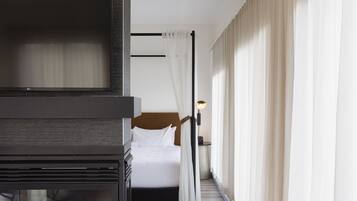 A modern hotel room with a fireplace, a bed, and a view of the city.