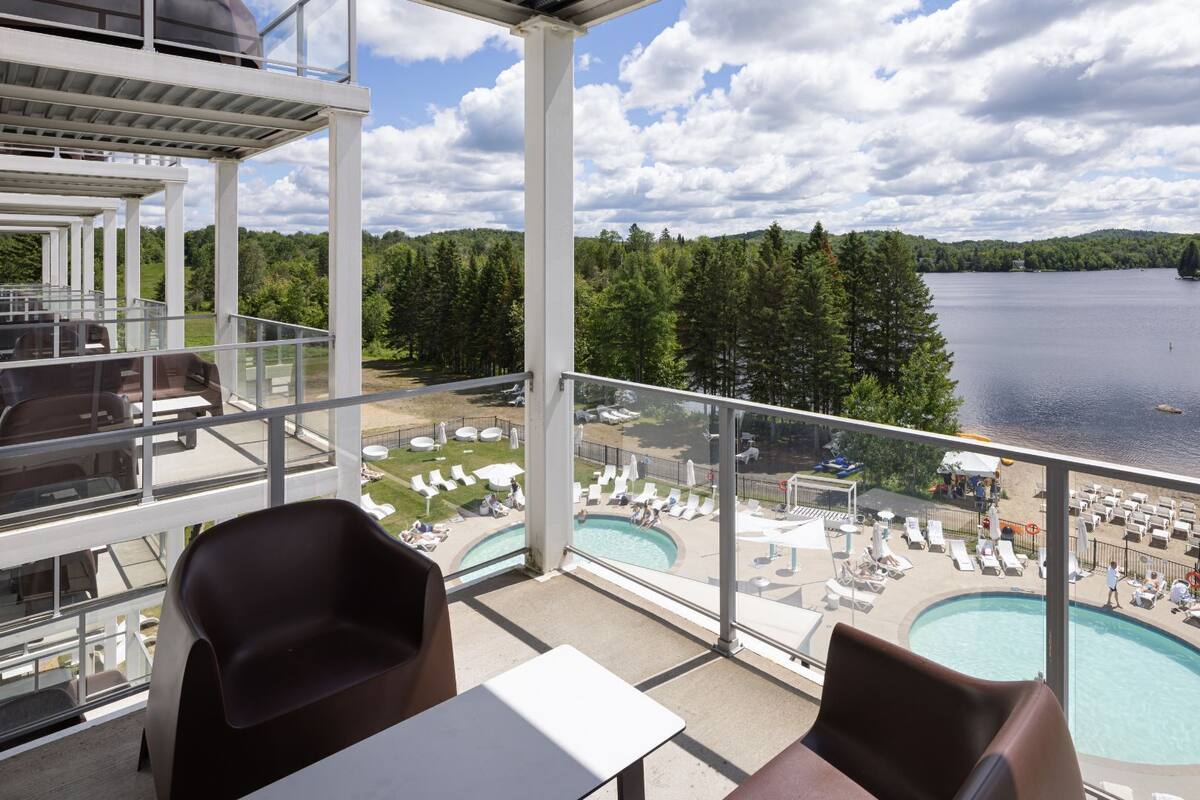 A balcony with a pool, lounge chairs, and a view of a lake and forest.