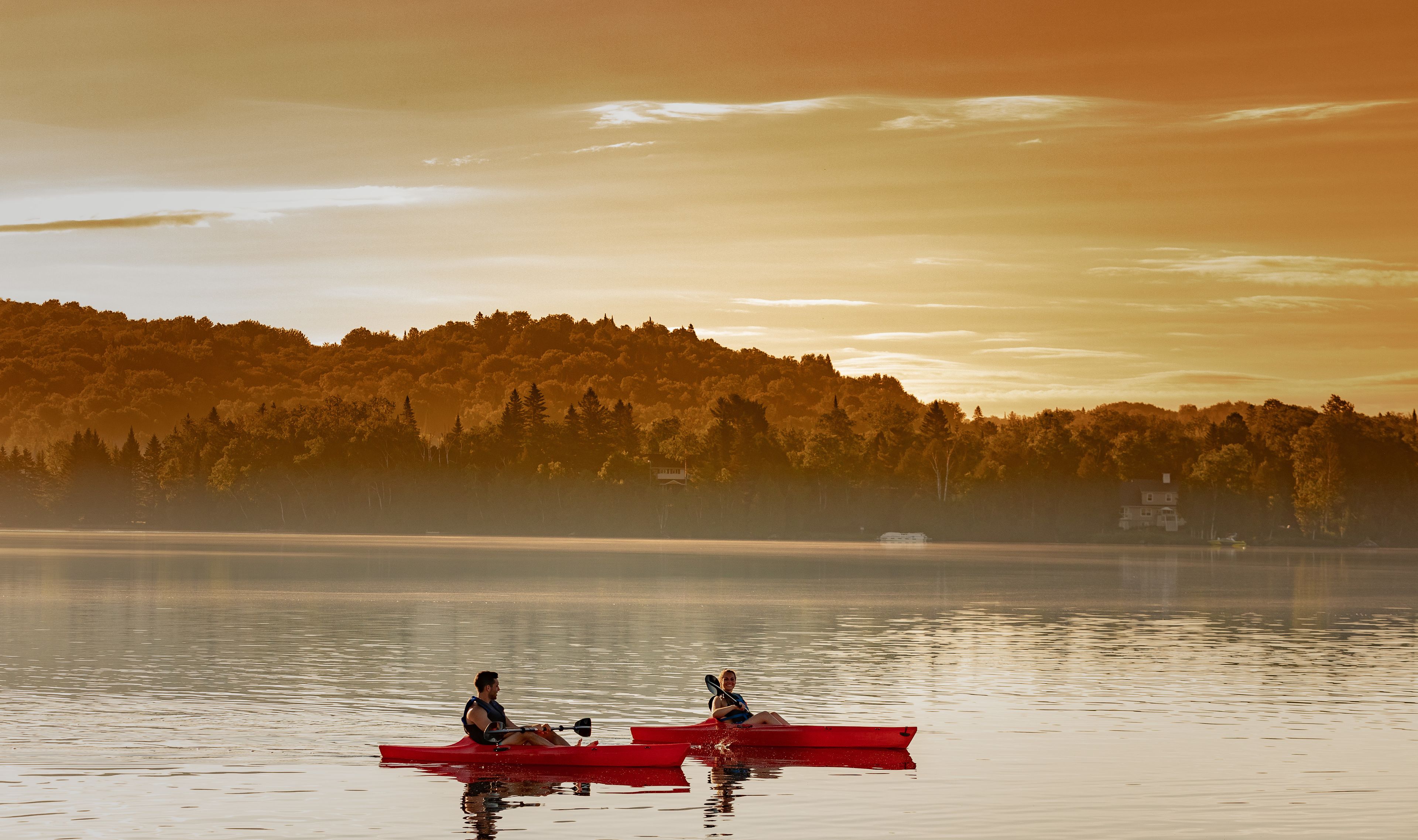 A calm lake with two kayaks, one red and one white, with people paddling.