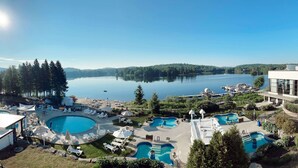 Ein Resort mit mehreren Schwimmbecken, einem großen See und einem modernen Gebäude mit Glasfassade.