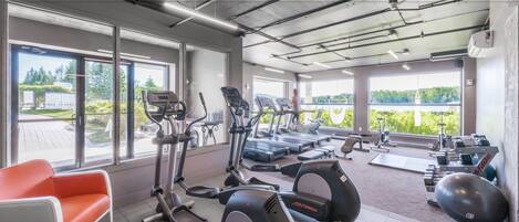 A gym with cardio machines, weight benches, and a bench with a view of the outdoors.