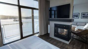 A modern hotel room with a large window, a fireplace, a flat-screen TV, and a bed.
