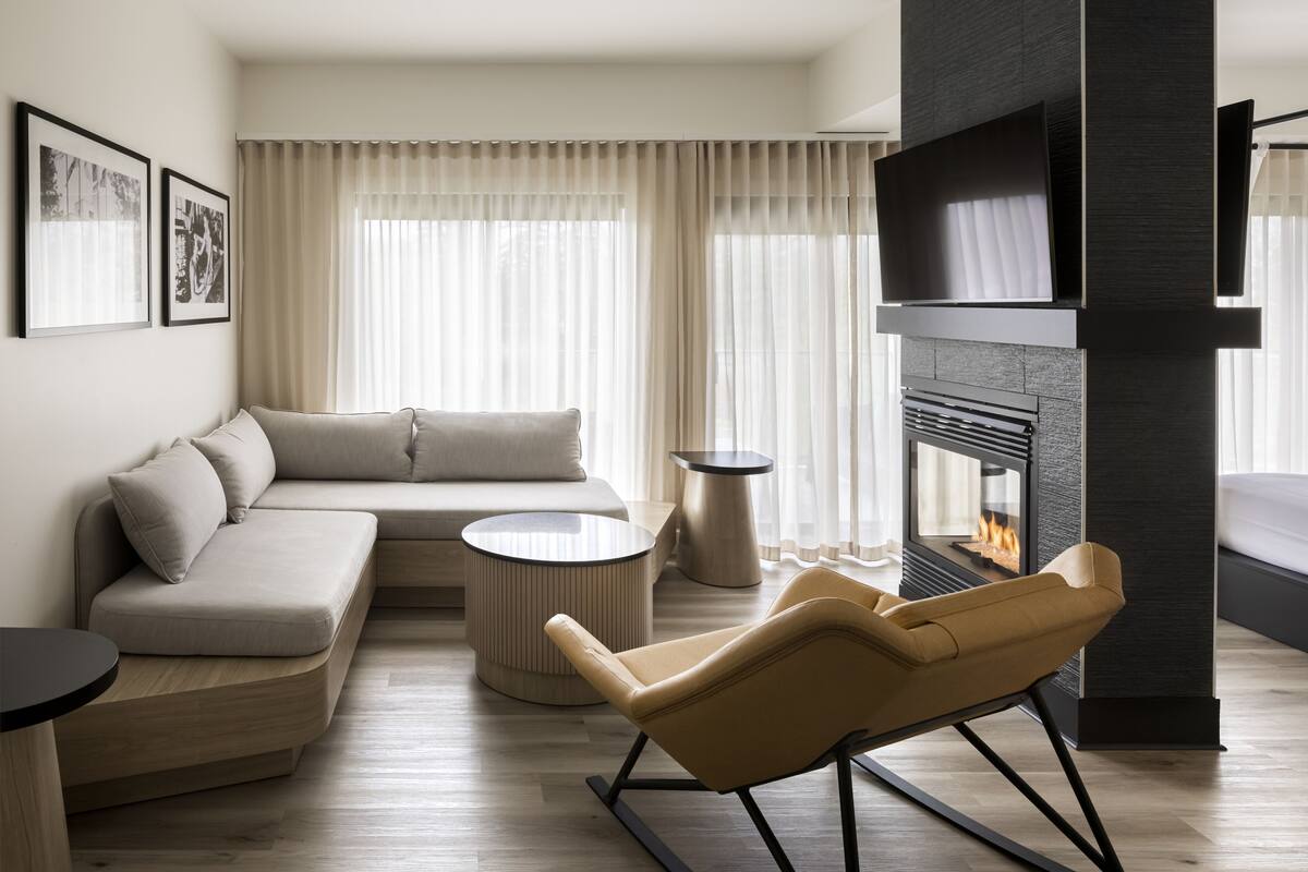 A modern living room with a sofa, a round coffee table, a leather chair, and a fireplace.