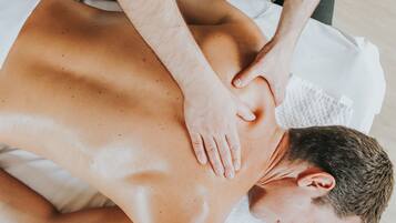 A person receiving a back massage on a bed with a white sheet.