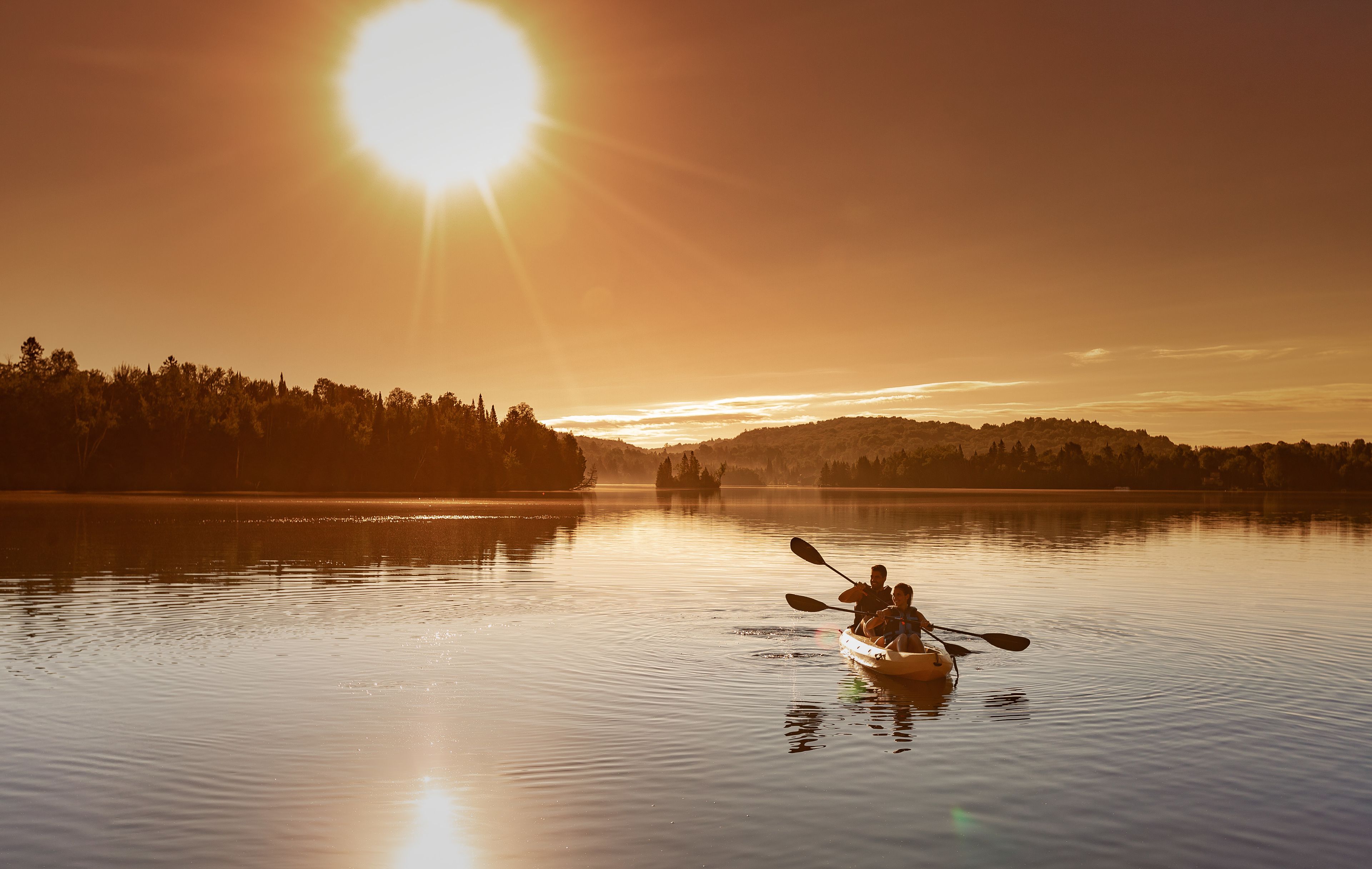 A calm lake at sunset with a kayak and two people paddling.