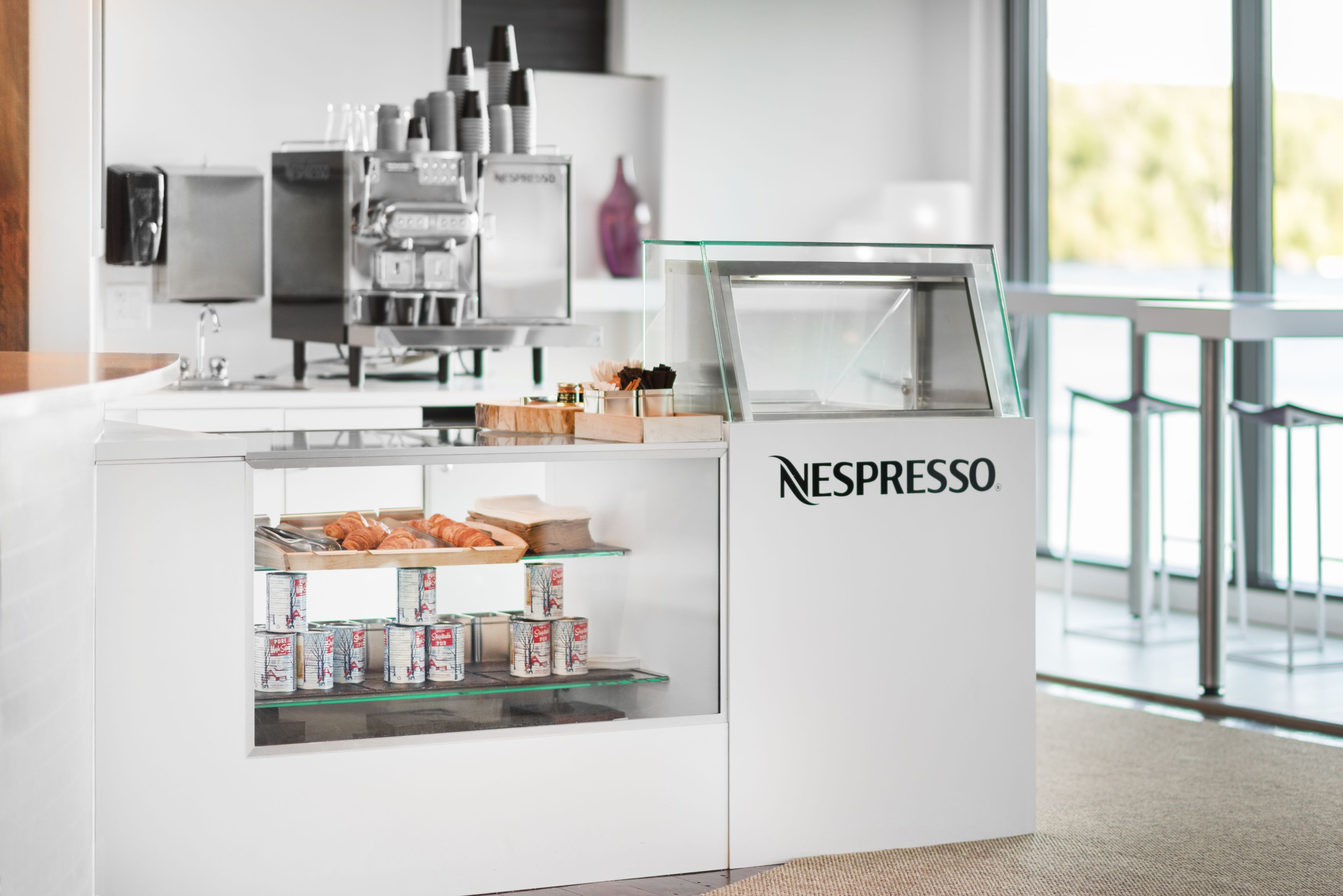 A modern Nespresso coffee station with a glass display case, espresso machines, and neatly arranged pastries and coffee cans.