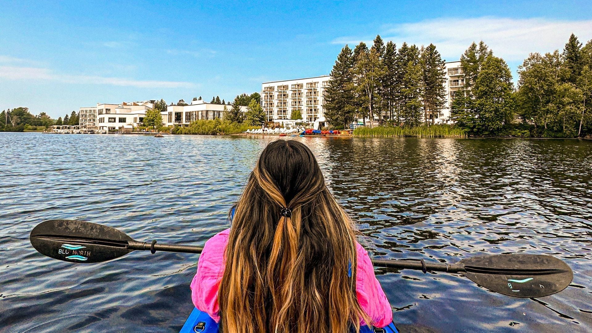 Une personne fait du kayak sur un lac, avec des bâtiments en arrière-plan.