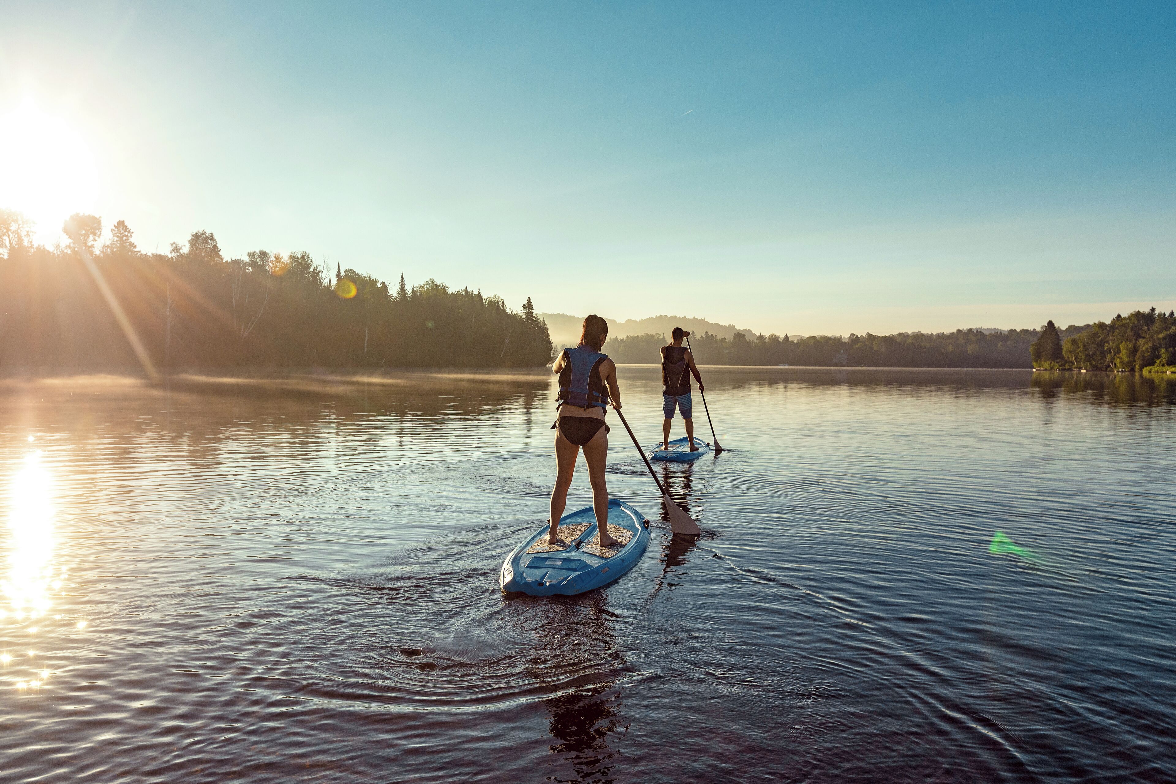 Deux personnes pratiquent le paddle sur un lac calme, avec des arbres en arrière-plan.