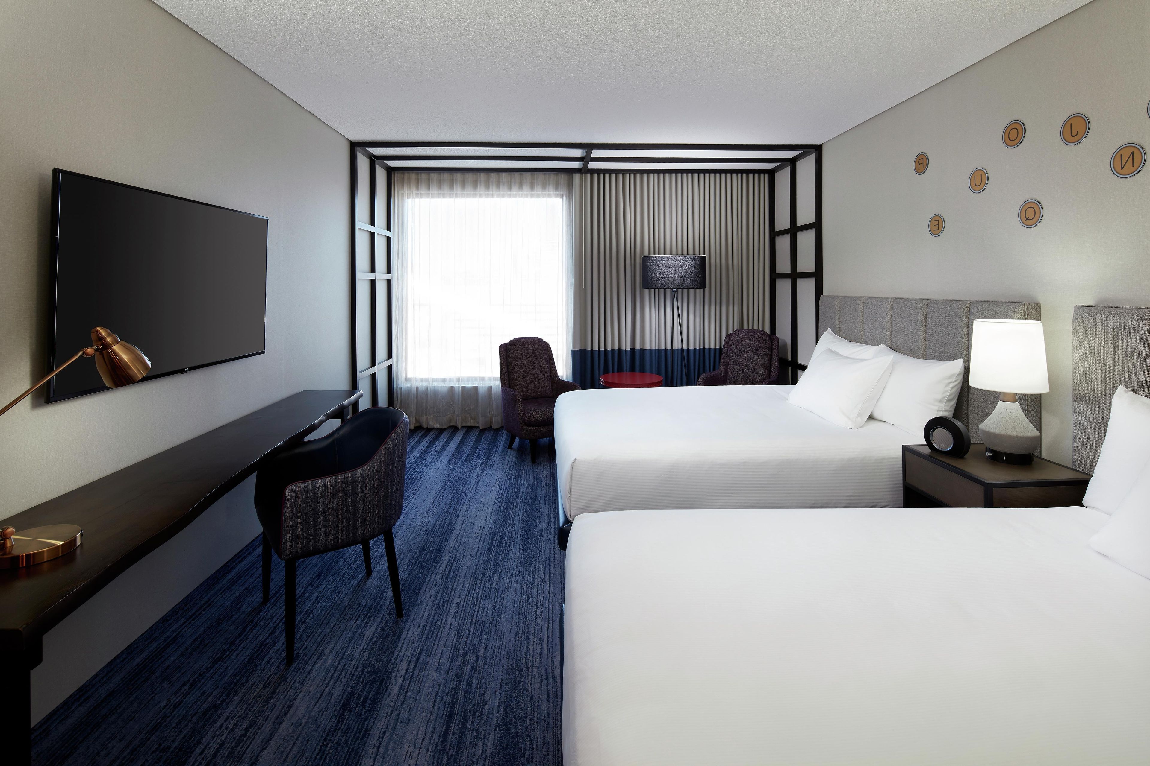 A hotel room with a bed, a desk, a chair, a TV, and a window with curtains.