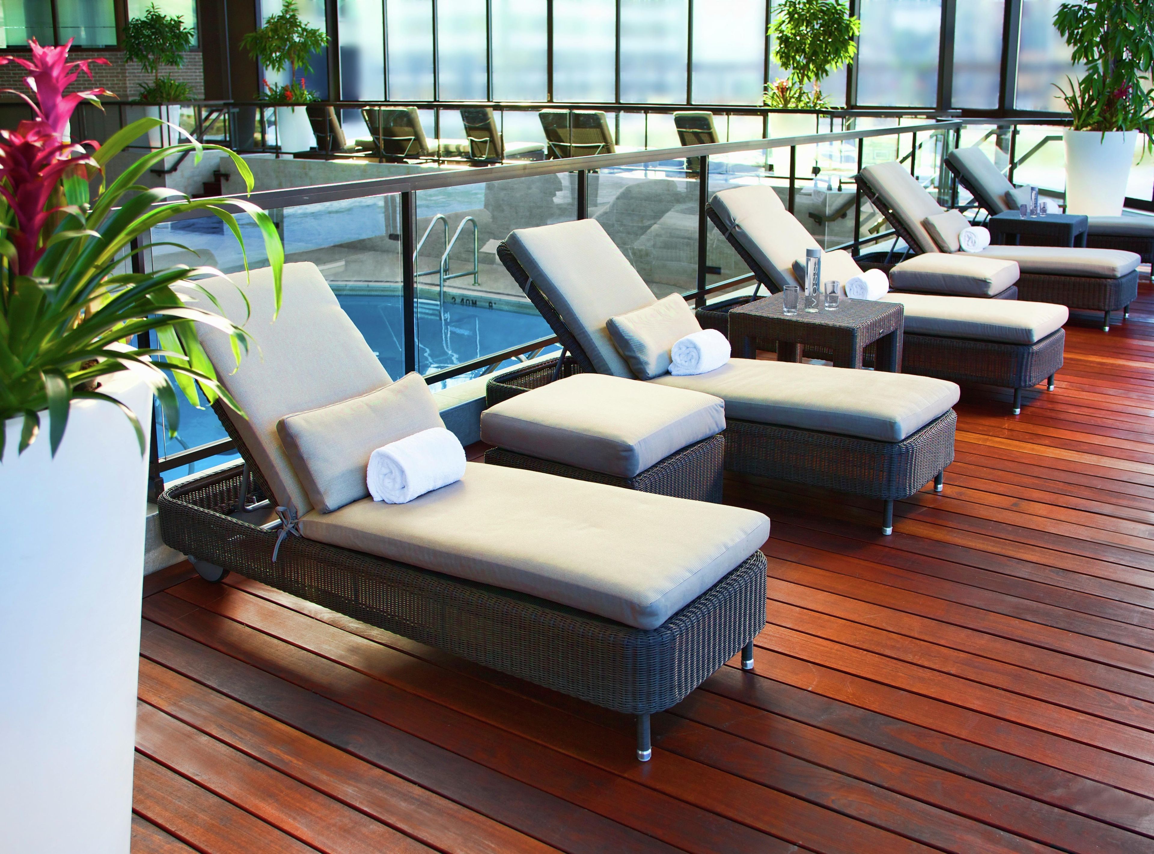 A sun deck with wicker lounge chairs, a pool, and potted plants.