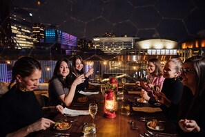 A group of people dining at a table with a city view, a red lantern, and a glass dome structure in the background. - DoubleTree by Hilton Montreal (Montreal)