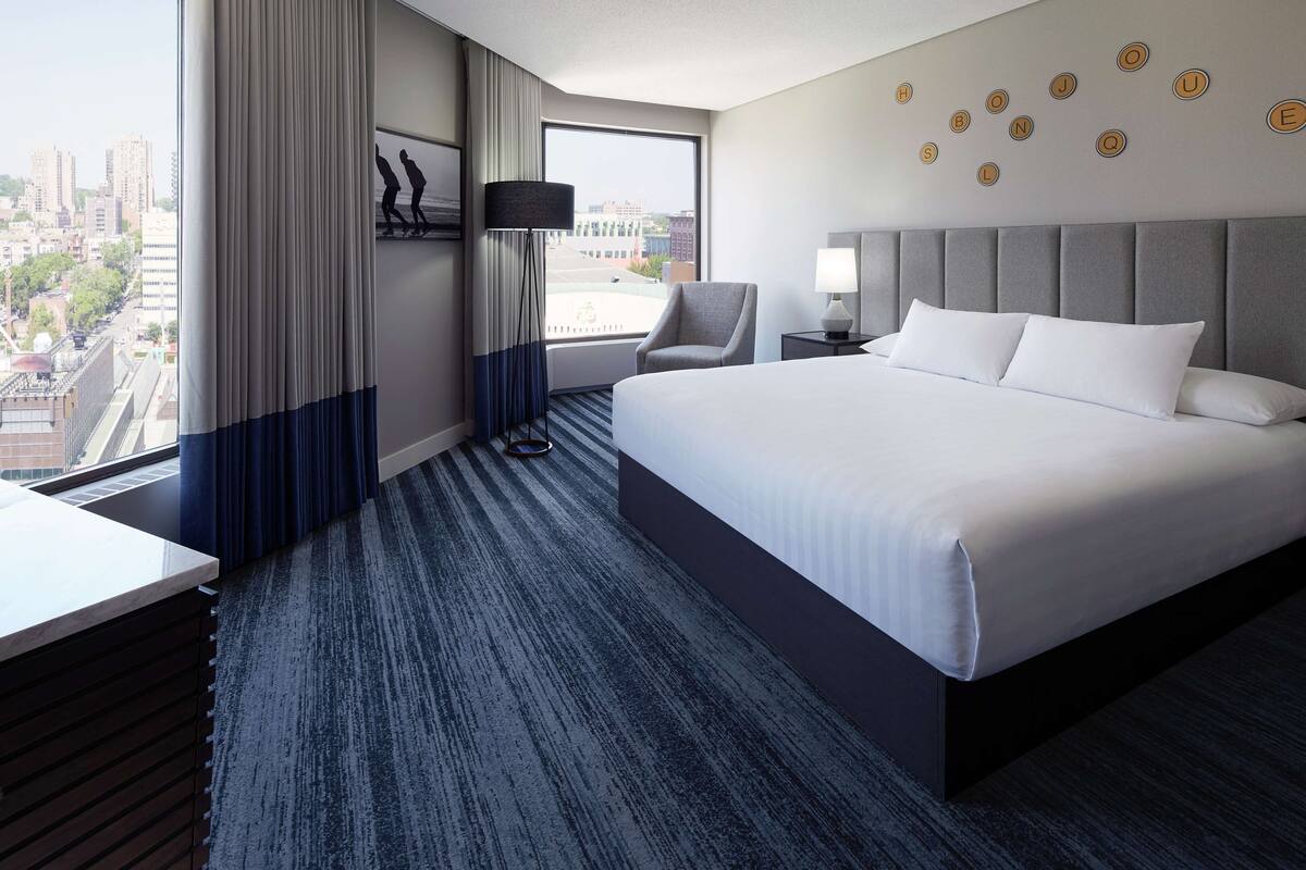 A hotel room with a large bed, a desk, a chair, and a view of the city.