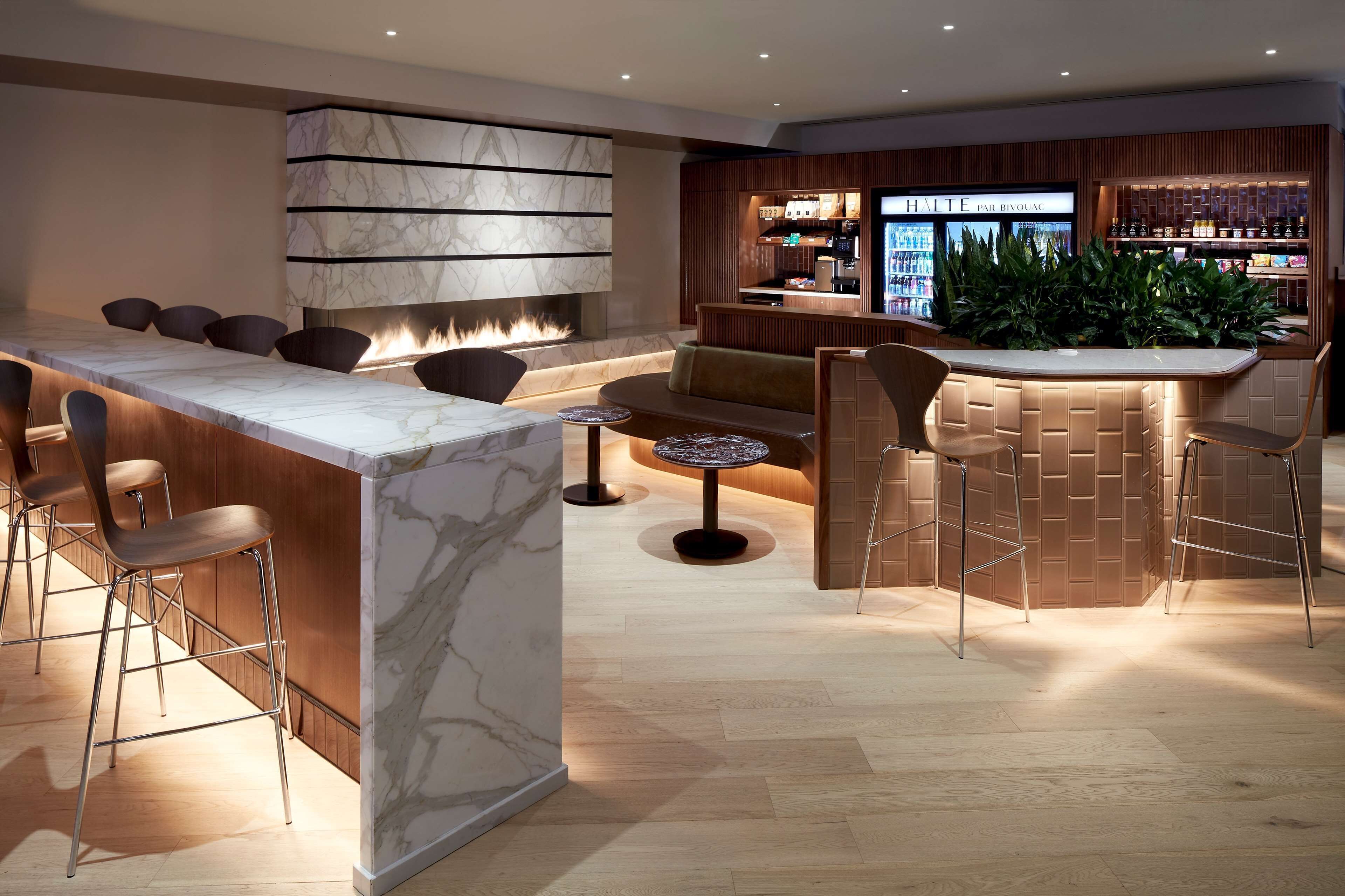 A modern bar area with marble countertops, bar stools, and a seating area with sofas and chairs.