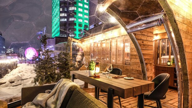 A cozy outdoor seating area with a wooden table and chairs, a small Christmas tree, and a view of a cityscape at night. - DoubleTree by Hilton Montreal (Montreal)