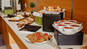 A buffet with various food items including cookies, fruits, and pastries.