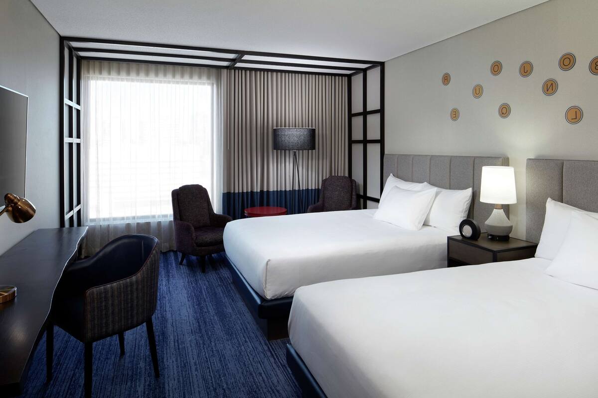 A hotel room with two beds, a desk, a chair, a lamp, and a wall with circular decorations.