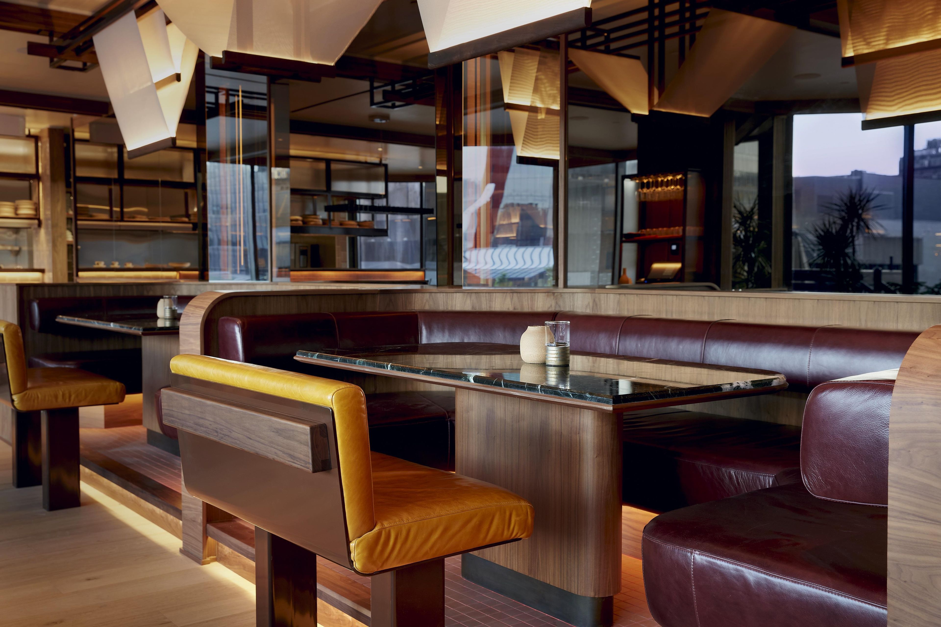 Interior moderno de restaurante con cabinas de madera, barra de mármol y vistas a la ciudad.