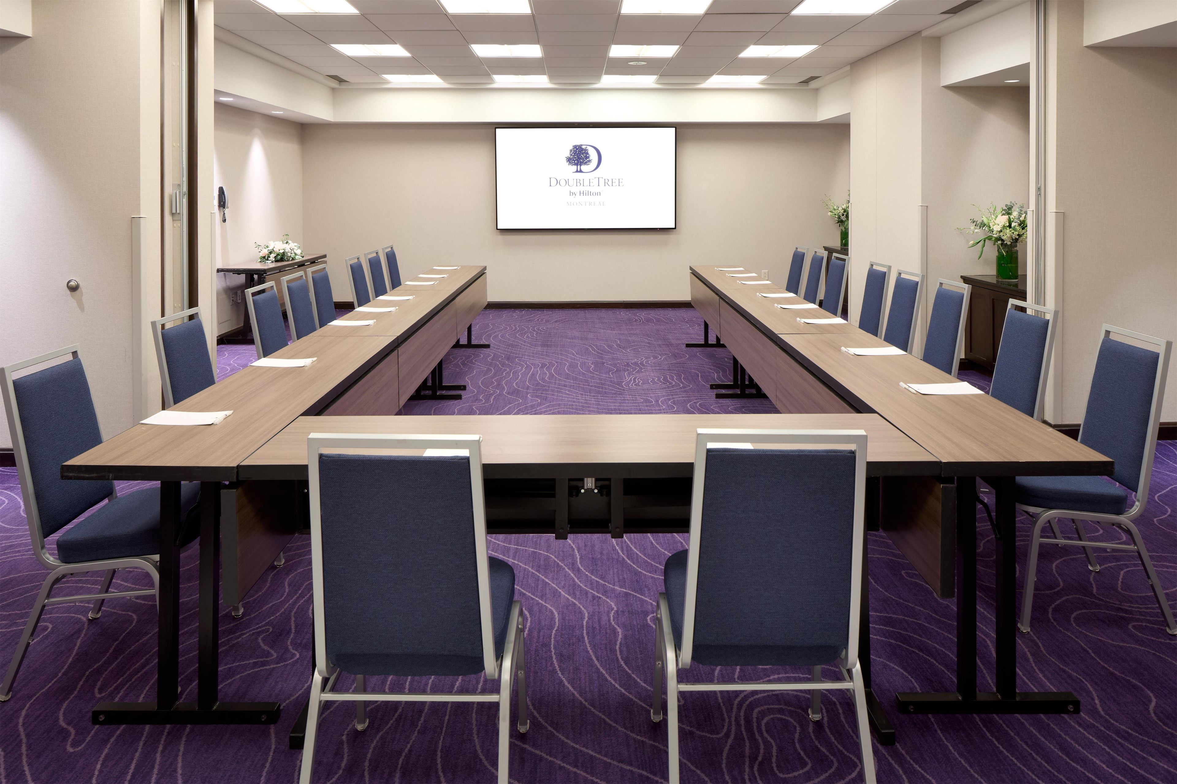 A conference room with a long table, blue chairs, and a projector screen displaying the DoubleTree logo.