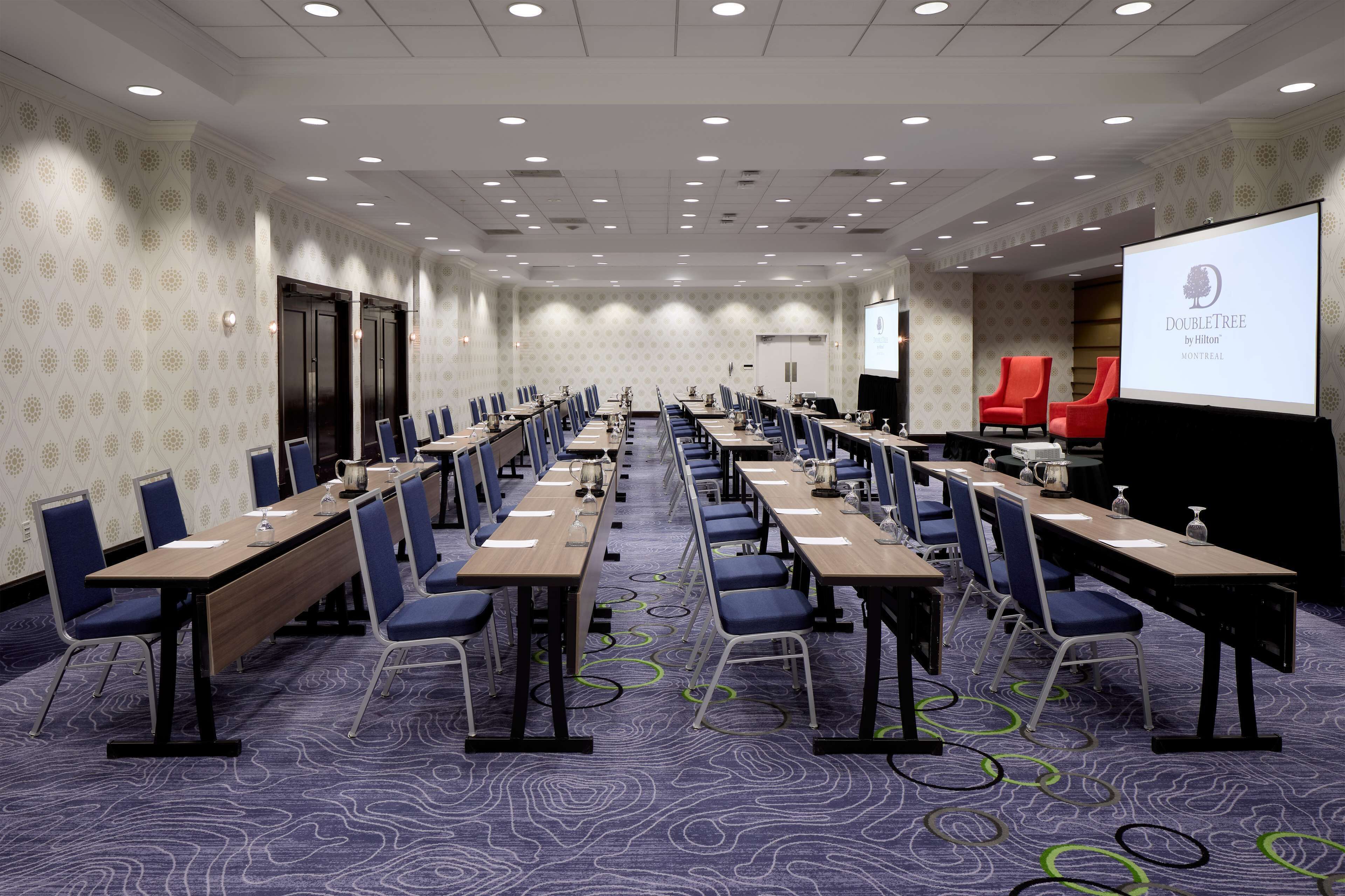 A conference room with multiple tables and chairs, a projector screen, and a presentation on the wall.