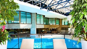 A modern indoor pool area with two lounge chairs, a glass barrier, and a view of the building's interior. - DoubleTree by Hilton Montreal (Montreal)