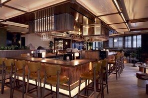 A bar area with a long counter, multiple stools, and a variety of bottles and glasses. - DoubleTree by Hilton Montreal (Montreal)
