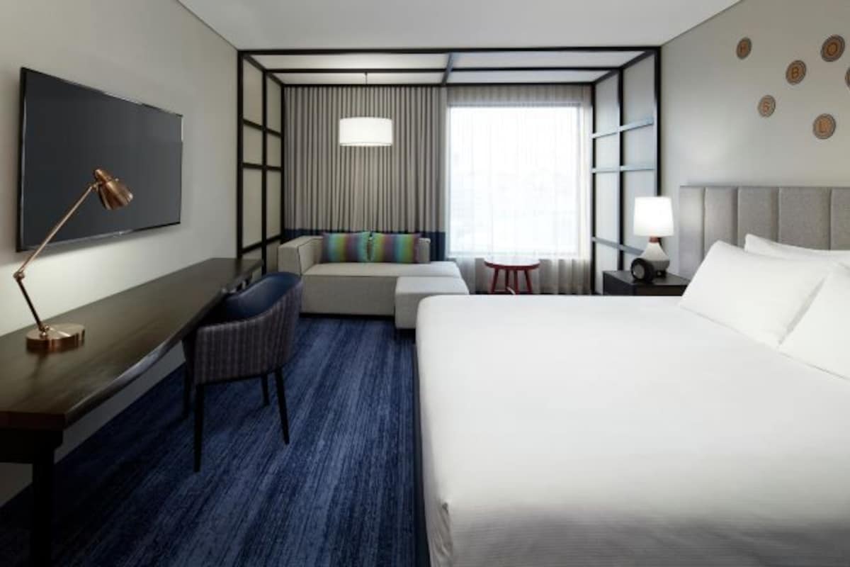 A hotel room with a large bed, a desk with a chair, a TV, and a window with curtains.
