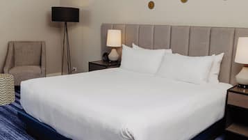Une chambre d’hôtel avec un grand lit, une chaise, une lampe sur pied, une table de chevet avec une lampe, et un mur décoré de motifs circulaires.