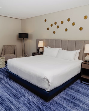 A hotel room with a large bed, a chair, a floor lamp, a nightstand with a lamp, and a wall with circular decorations.