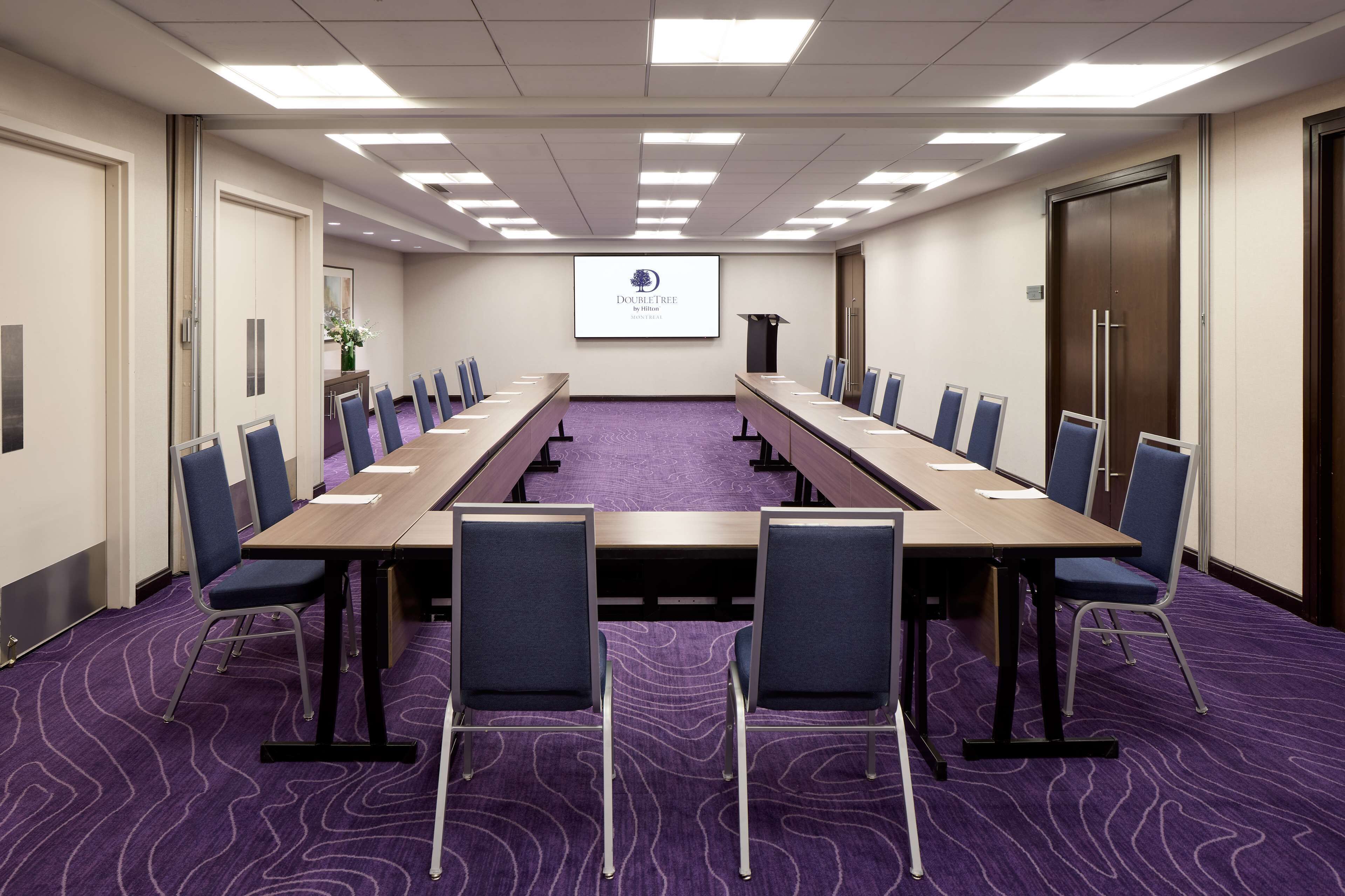 A conference room with a long table, chairs, a projector screen, and a purple carpet.