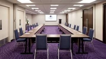 A conference room with a long table, chairs, a projector screen, and a purple carpet.