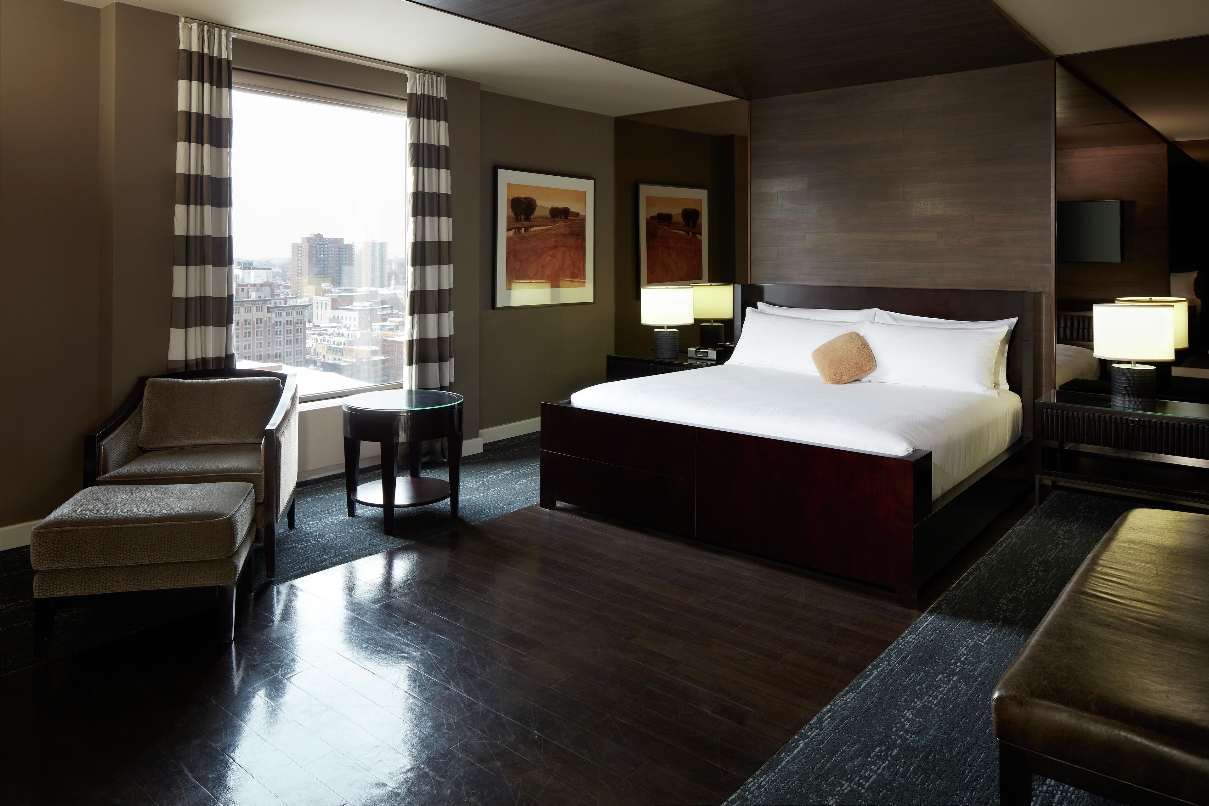 A hotel room with a large bed, a chair, a desk, and a view of the city.