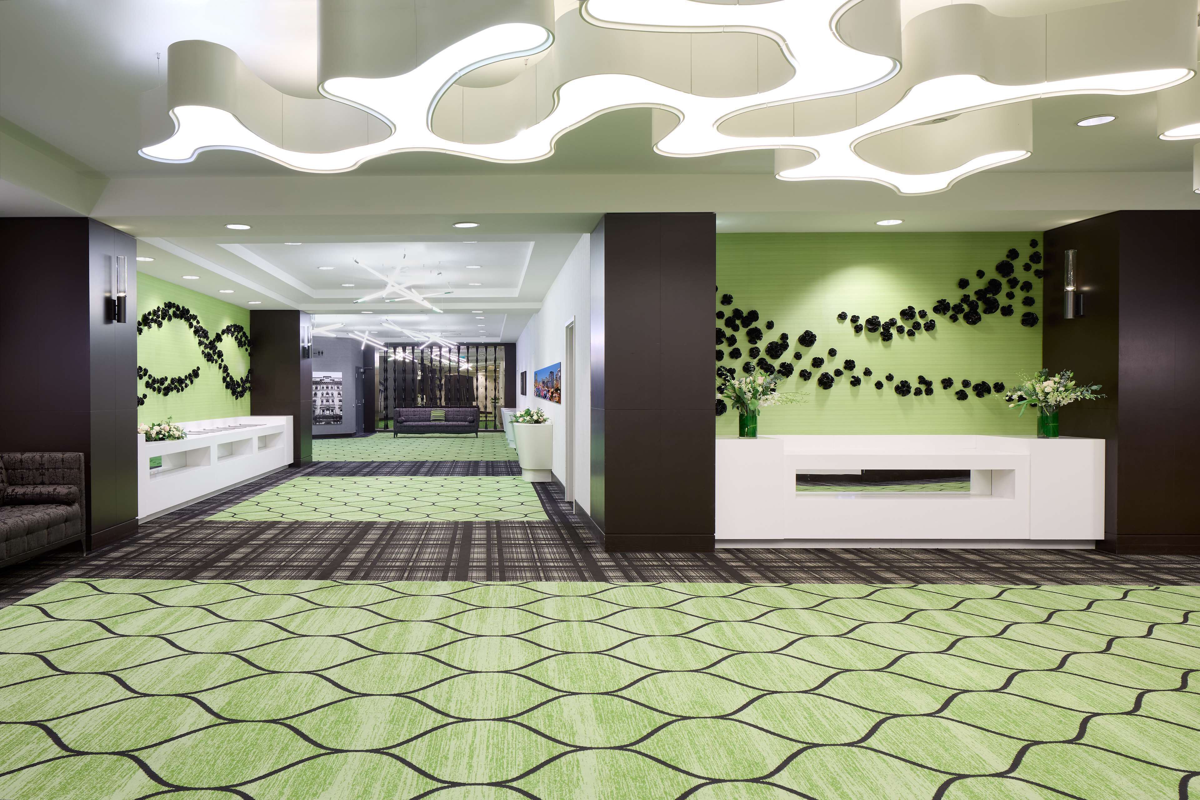 En moderne lobby med et grønt mønstret tæppe, en receptionsdisk og en væg dekoreret med sorte blomster.